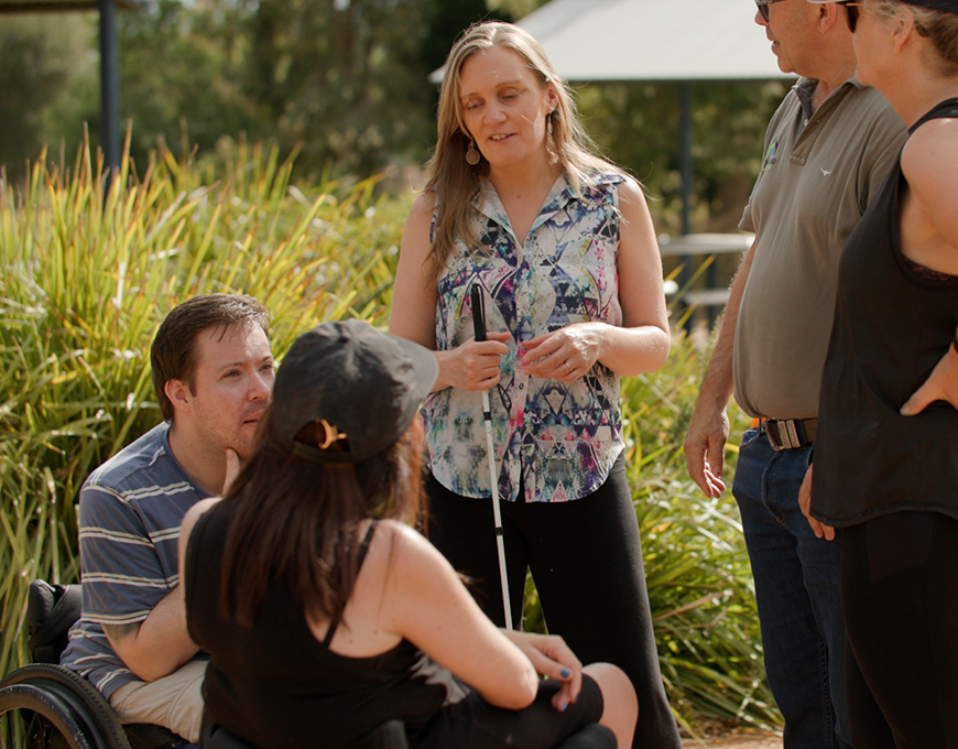 Mark and Cassie are standing with a vision impaired client and two clients in wheelchairs